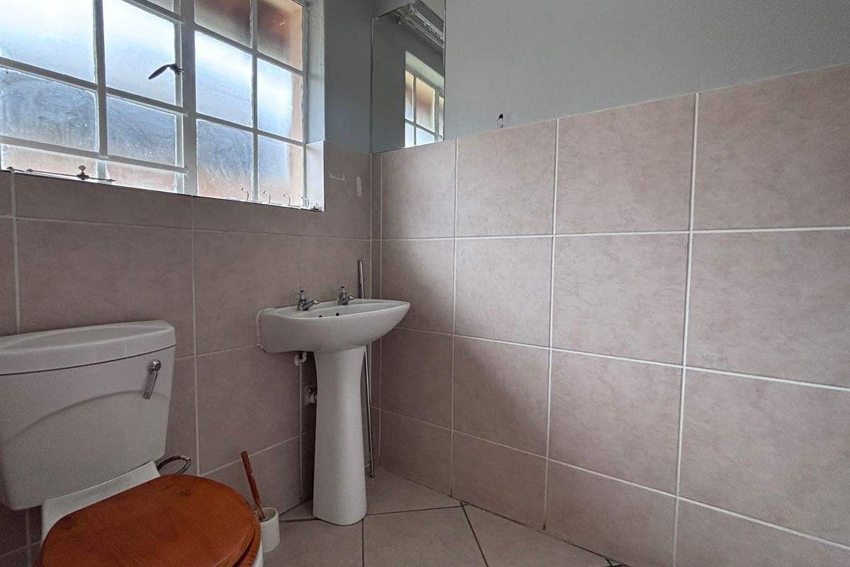 A functional bathroom featuring a pedestal sink, toilet, and neutral wall tiling. The space is currently vacant and ready for updates.