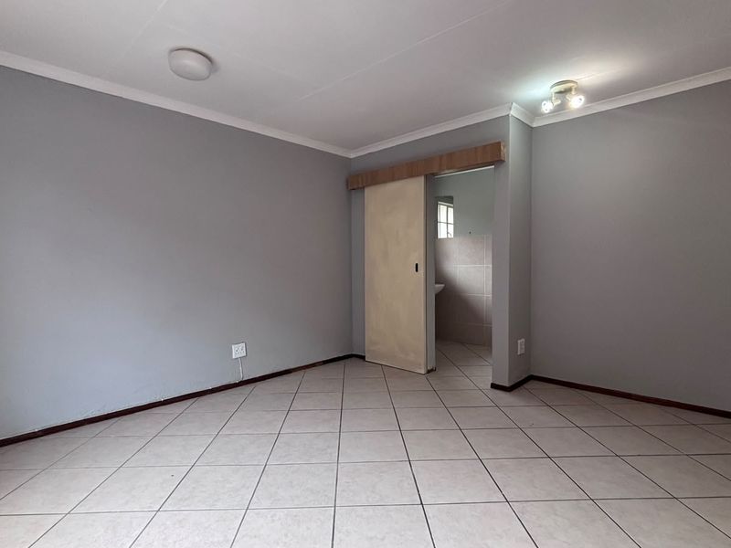 A clean, empty bedroom featuring neutral grey walls, tiled flooring, and a sliding door leading to an adjoining space.