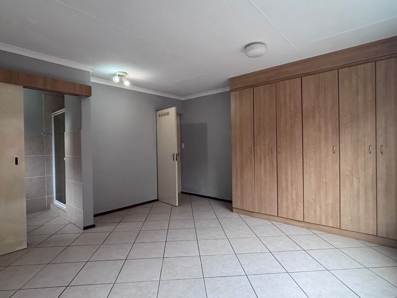 A spacious bedroom featuring neutral tiled flooring, extensive built-in wooden cupboards, and direct access to an en-suite bathroom.