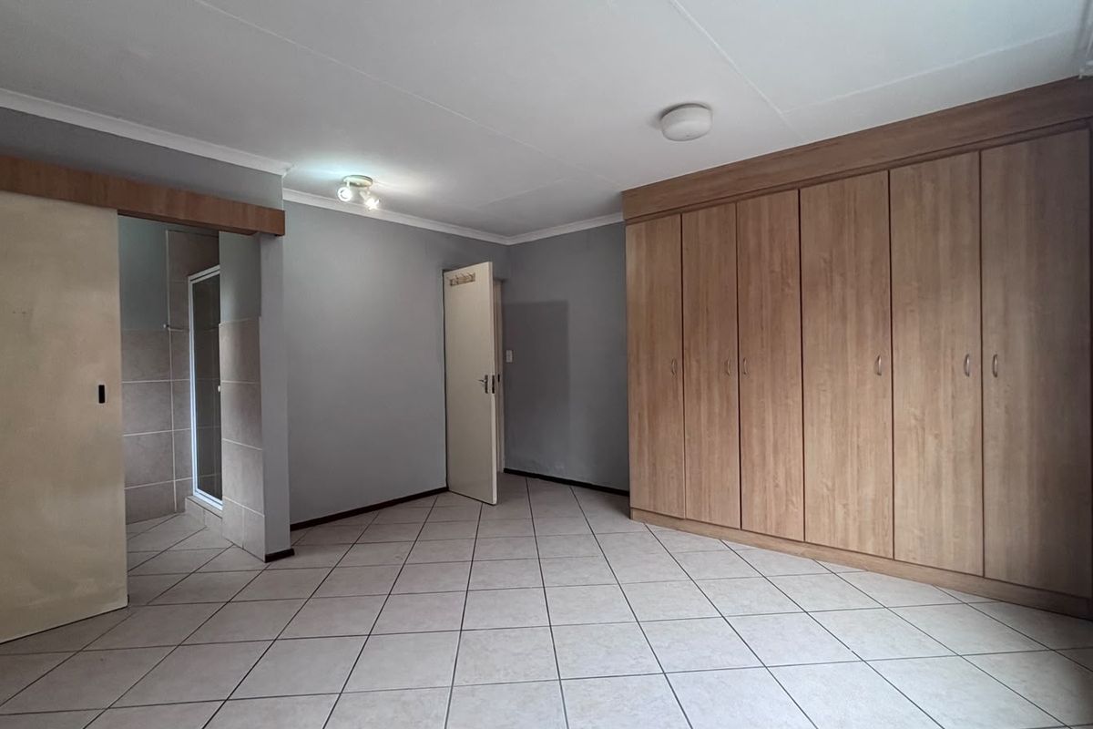 A spacious bedroom featuring neutral tiled flooring, extensive built-in wooden cupboards, and direct access to an en-suite bathroom.