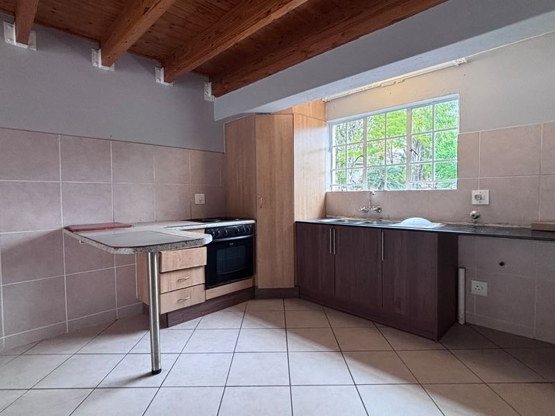 A functional kitchen featuring exposed timber ceiling beams, laminate cabinetry, built-in oven, hob, and tiled finishes throughout.