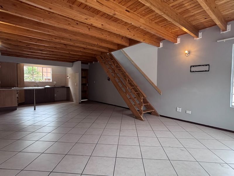 Spacious open-plan living area featuring exposed timber beam ceilings, tiled flooring, and an integrated kitchen space with a timber staircase.