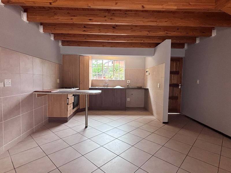 An open-plan kitchen featuring exposed timber ceiling beams, tiled flooring, built-in cabinetry with laminate countertops, and a tiled splashback.