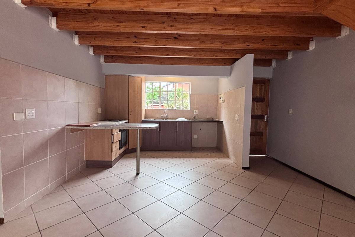 An open-plan kitchen featuring exposed timber ceiling beams, tiled flooring, built-in cabinetry with laminate countertops, and a tiled splashback.
