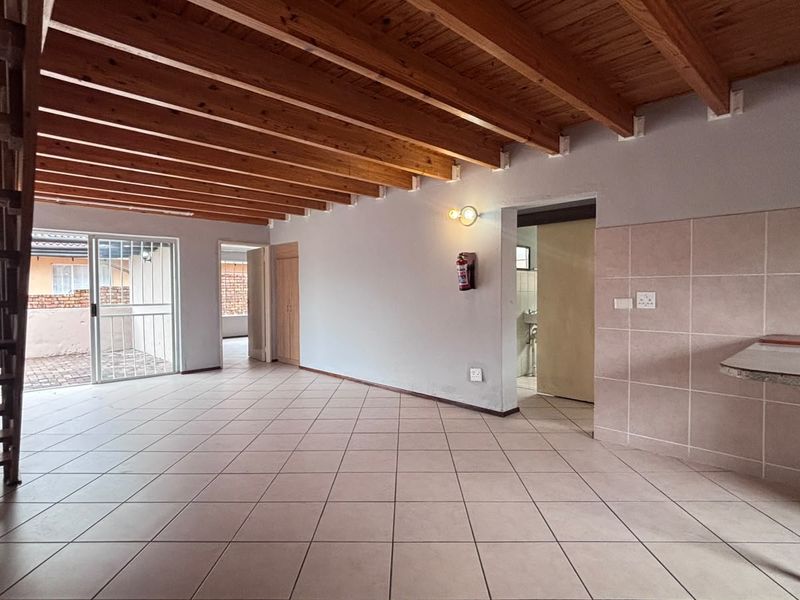 Spacious open-plan living area featuring exposed timber ceiling beams, tiled flooring, and a built-in breakfast counter with direct access to the exterior.