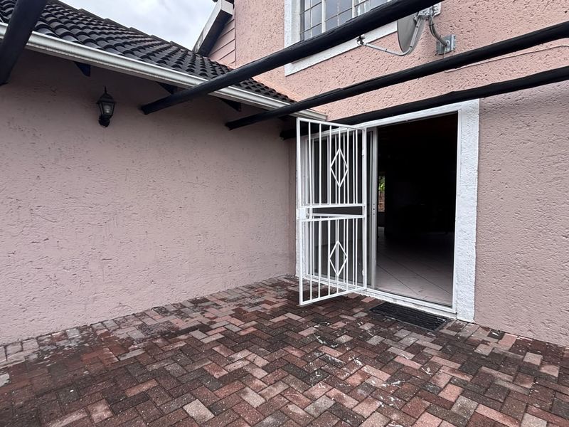 A paved outdoor patio area featuring a security gate and sliding door access to the interior, with a covered roof structure.