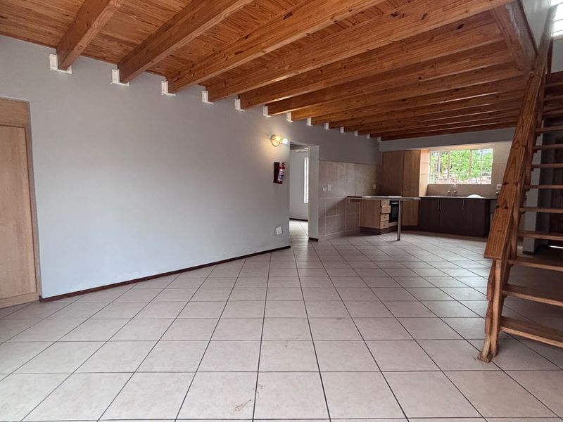 Spacious open-plan living and kitchen area featuring exposed timber ceiling beams, tiled flooring, and a wooden staircase leading to the upper level.