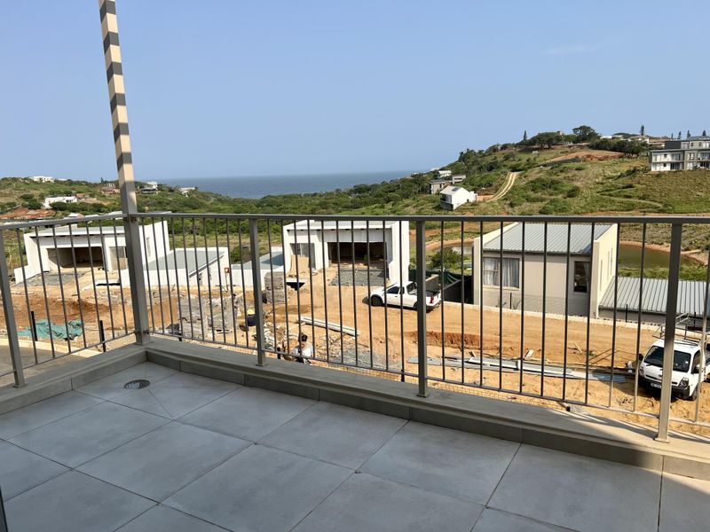 A modern balcony featuring tiled flooring and a metal balustrade, offering elevated views of the surrounding landscape and coastal area.
