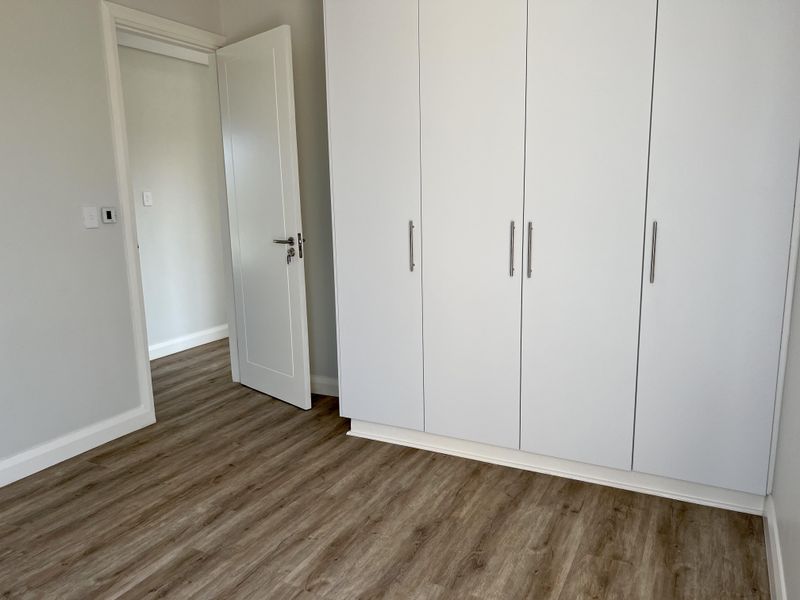 A bright, modern bedroom featuring neutral walls, high-quality laminate flooring, and ample built-in wardrobe storage.