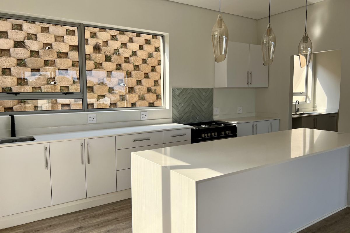 Modern kitchen featuring a central island, quartz countertops, gas stove, herringbone backsplash, and sleek cabinetry, complemented by contemporary pendant lighting.