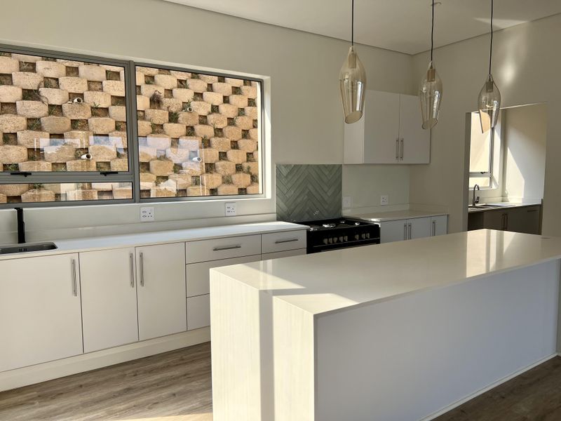 Modern kitchen featuring a central island, quartz countertops, gas stove, herringbone backsplash, and sleek cabinetry, complemented by contemporary pendant lighting.