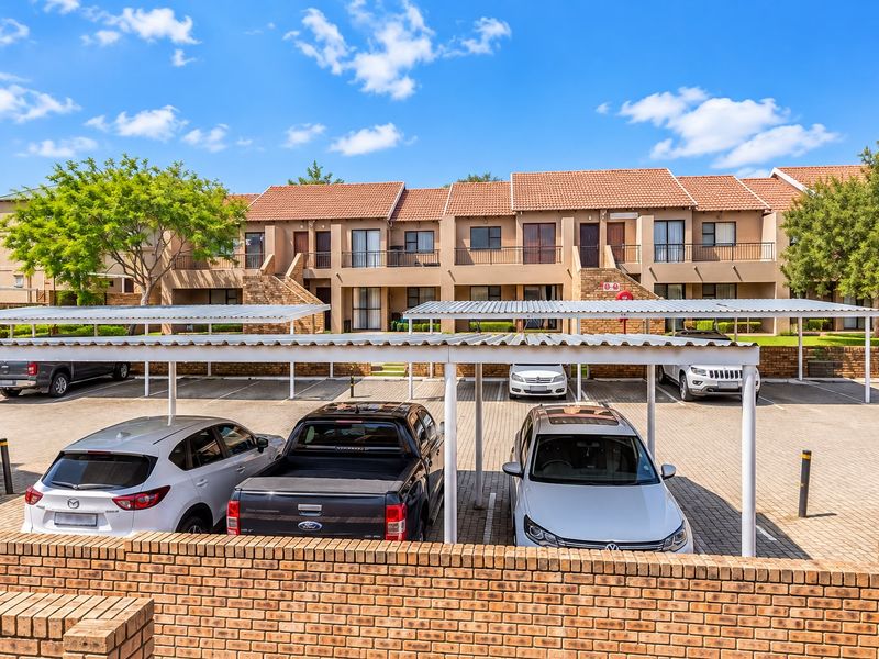 Exterior view of an apartment complex featuring covered parking bays, paved driveway, and multi-level units with balconies.
