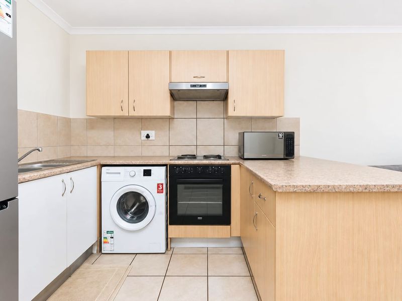 Compact kitchen featuring light wood-finish cabinetry, laminate countertops, tiled backsplash, and integrated appliances including an oven, hob, and extractor fan.