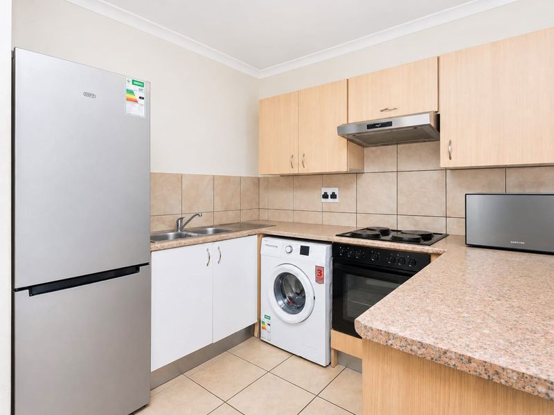 A functional kitchen featuring light wood-finish cabinetry, stone-look countertops, tiled backsplash, and integrated appliances including an oven, hob, and extractor fan.