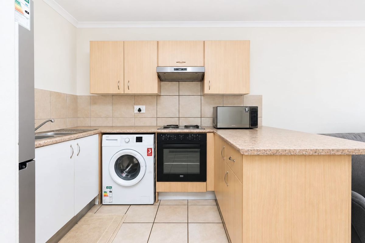 Compact kitchen featuring light wood-finish cabinetry, laminate countertops, tiled backsplash, and integrated appliances including an oven, hob, and extractor fan.