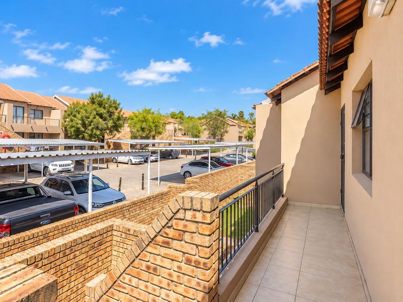 A clean, tiled balcony featuring a brick wall and metal railing, overlooking the apartment complex parking area.