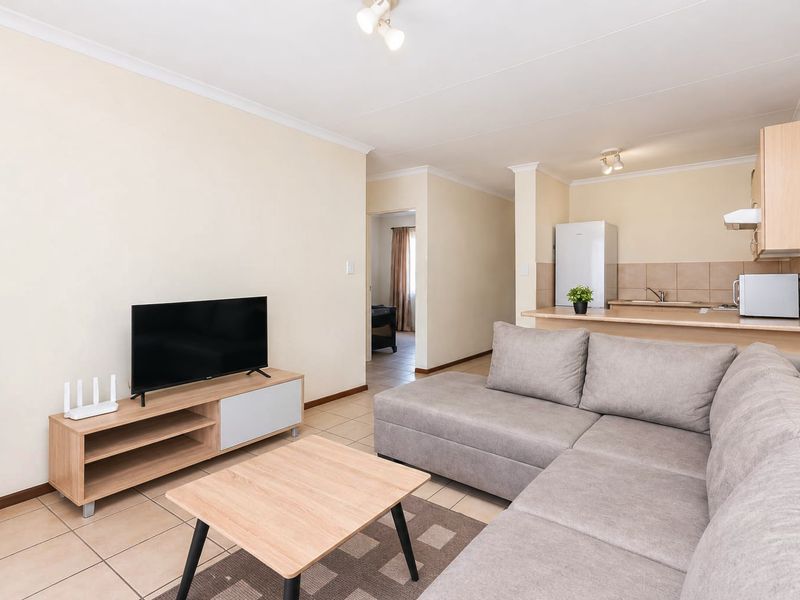 Open-plan living area featuring tiled floors, a breakfast counter, and a functional kitchen with built-in cabinetry and an extractor fan.
