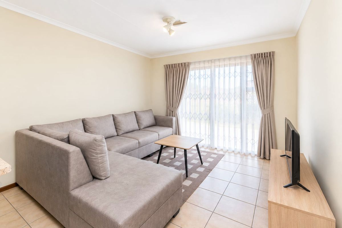 A bright and well-maintained living room featuring neutral tiled flooring, a sliding glass door with security gate, and clean, light-toned walls.