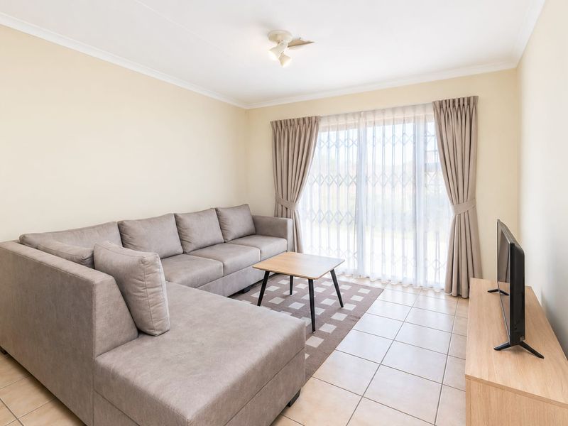 A bright and well-maintained living room featuring neutral tiled flooring, a sliding glass door with security gate, and clean, light-toned walls.