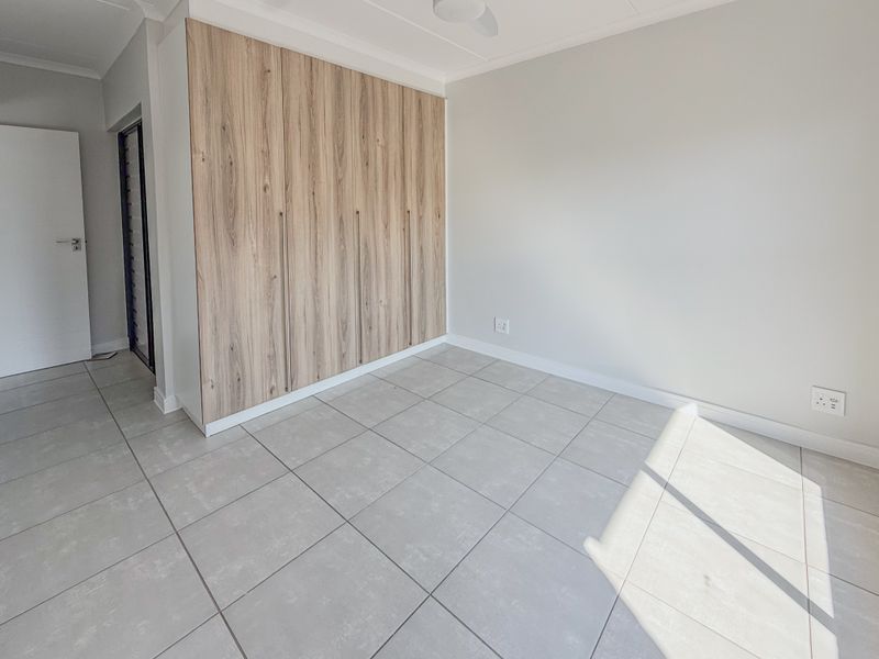 A bright, empty bedroom featuring modern light wood-grain built-in cupboards and neutral floor tiles, offering a clean and versatile space.