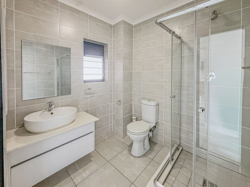 A modern, well-maintained bathroom featuring neutral floor-to-ceiling tiling, a sleek vanity with a vessel sink, and a glass-enclosed shower.