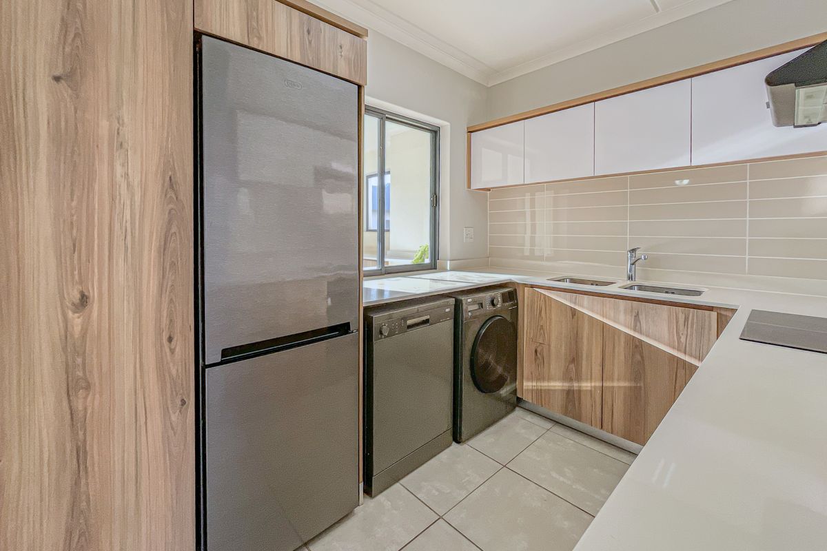 Modern kitchen featuring wood-grain and white cabinetry, stone countertops, tiled backsplash, and integrated space for appliances.