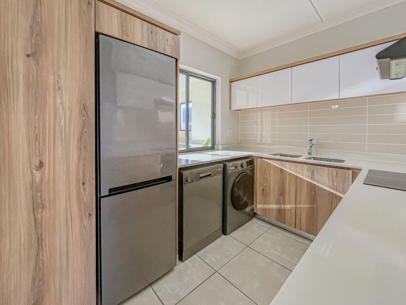 Modern kitchen featuring wood-grain and white cabinetry, stone countertops, tiled backsplash, and integrated space for appliances.