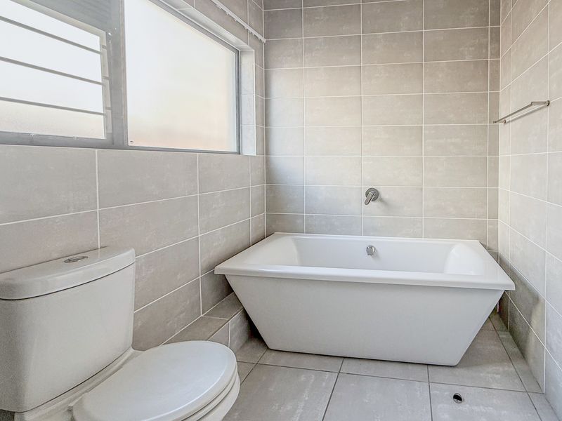 A clean, modern bathroom featuring a freestanding bathtub, neutral wall and floor tiling, and a toilet.