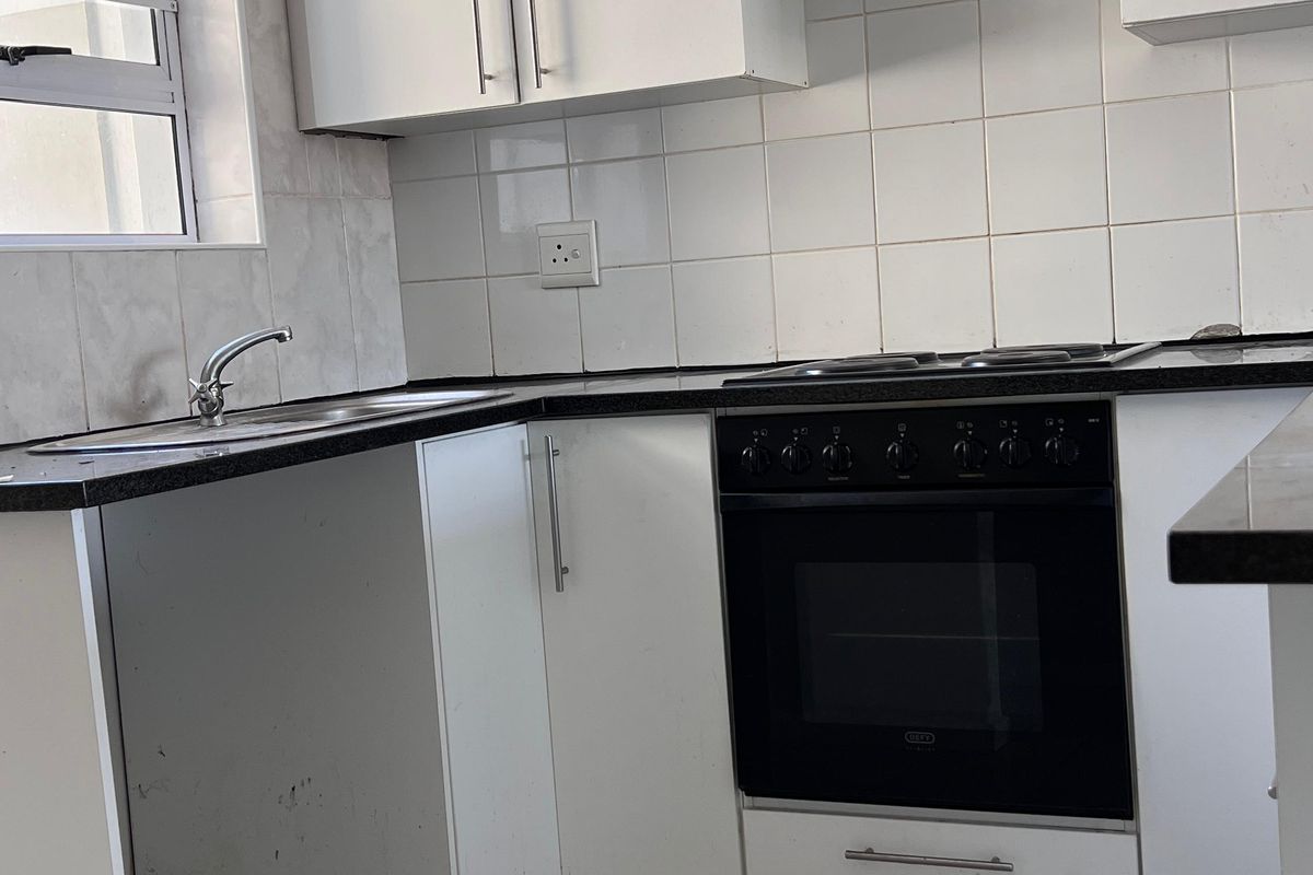 A functional kitchen featuring white cabinetry, black granite countertops, a built-in oven with hob, and tiled finishes throughout.