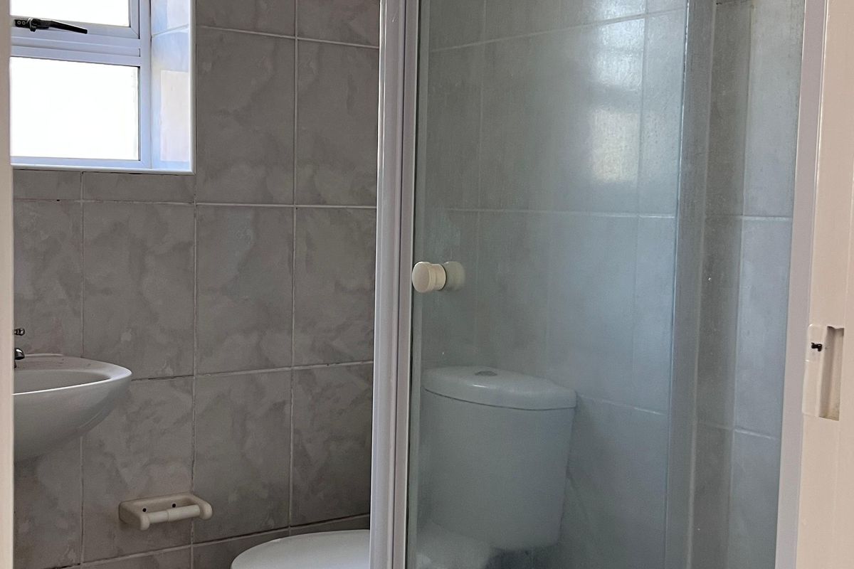 A functional bathroom featuring a shower enclosure, toilet, and wall-mounted basin with neutral tiled finishes throughout.