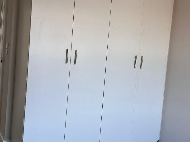 A bedroom featuring a large white built-in wardrobe and neutral tiled flooring, presenting a clean and functional space ready for personalization.