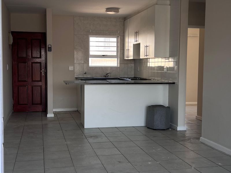 An open-plan living and kitchen area featuring tiled flooring, white cabinetry, and a breakfast counter, presenting a clean, blank canvas for personalization.