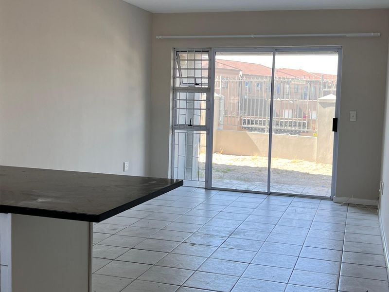 An empty open-plan living and kitchen area featuring tiled flooring, a kitchen island, and a sliding glass door leading to an outdoor space.