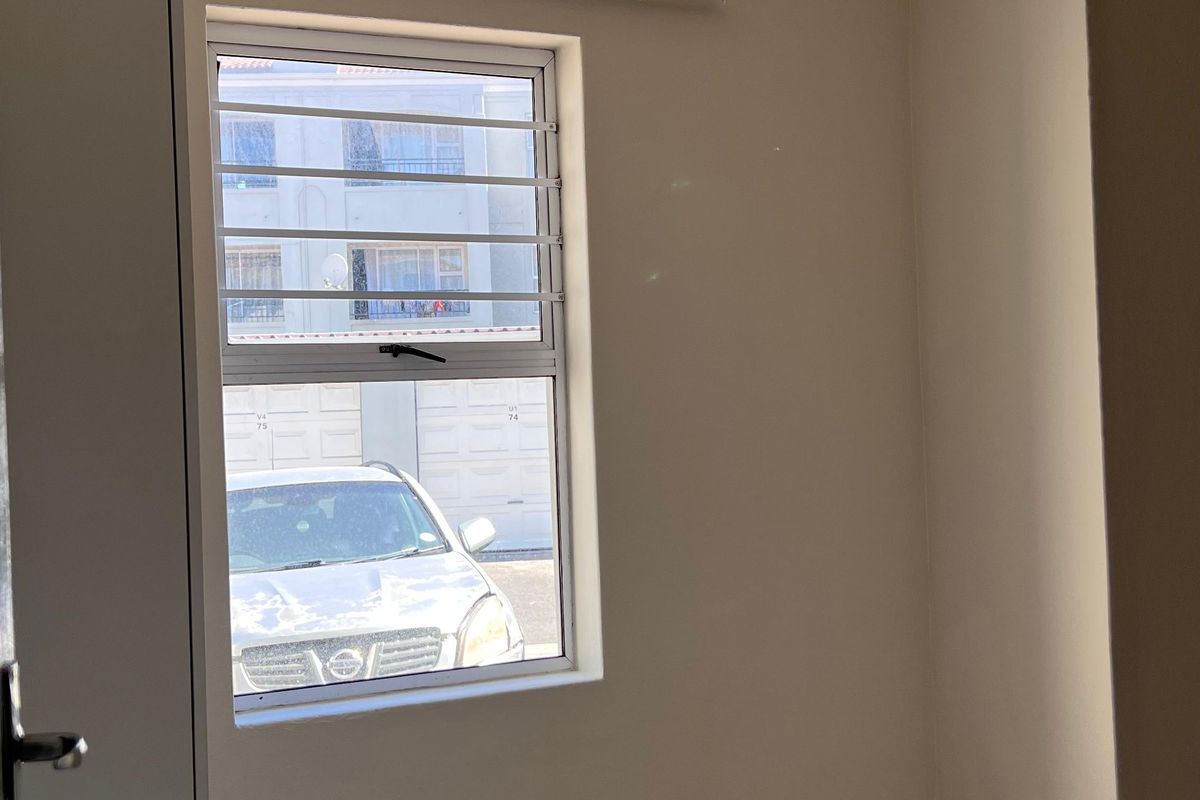 A vacant bedroom featuring neutral wall paint, tiled flooring, and a window fitted with security bars.