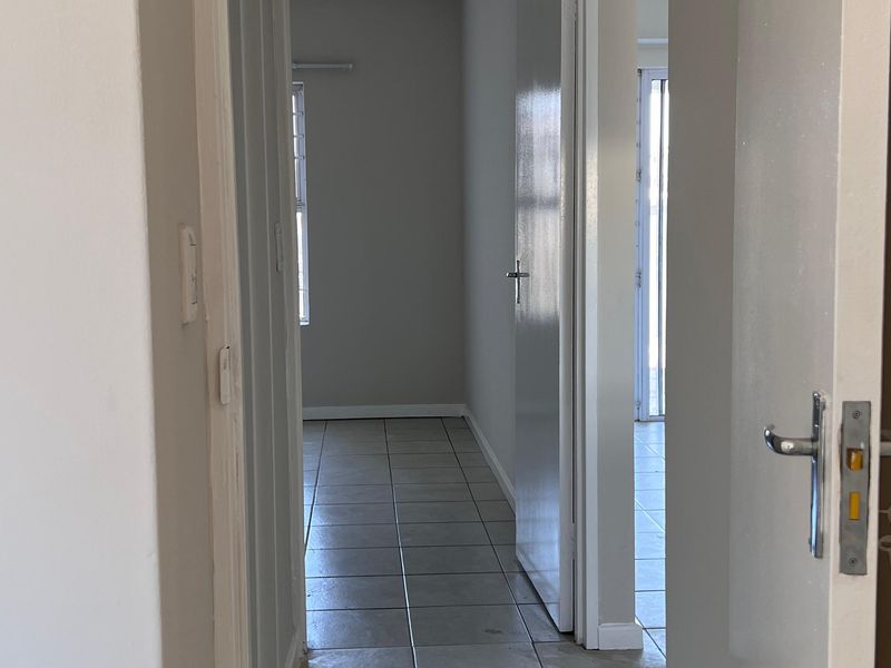 A vacant hallway featuring neutral wall paint and tiled flooring, providing access to adjacent rooms within the apartment.