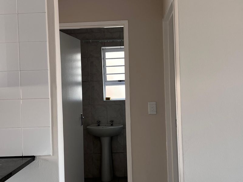 A view from a tiled hallway looking into a bathroom featuring a pedestal basin and louvered window.