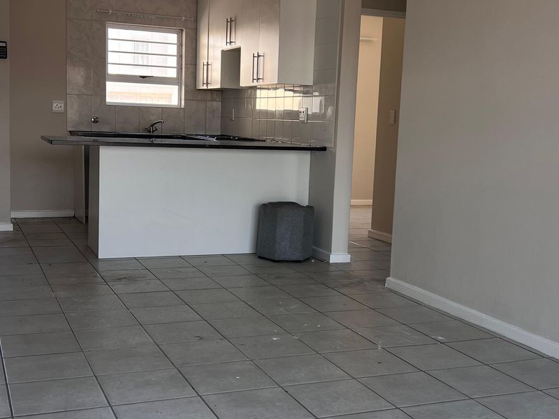 Open plan kitchen and living area featuring tiled flooring, white cabinetry, and a breakfast bar island in a neutral, vacant space.