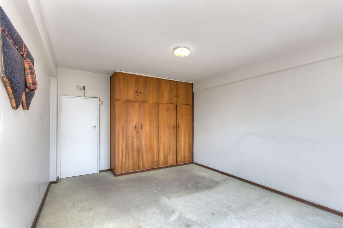 A vacant bedroom featuring built-in wooden wardrobes, neutral walls, and carpet flooring, offering a blank canvas for renovation or restyling.