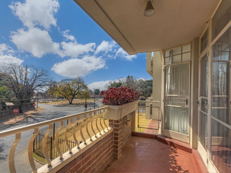 A covered balcony featuring a brick balustrade, metal railing, and security gate, offering an elevated view of the surrounding street and neighborhood.