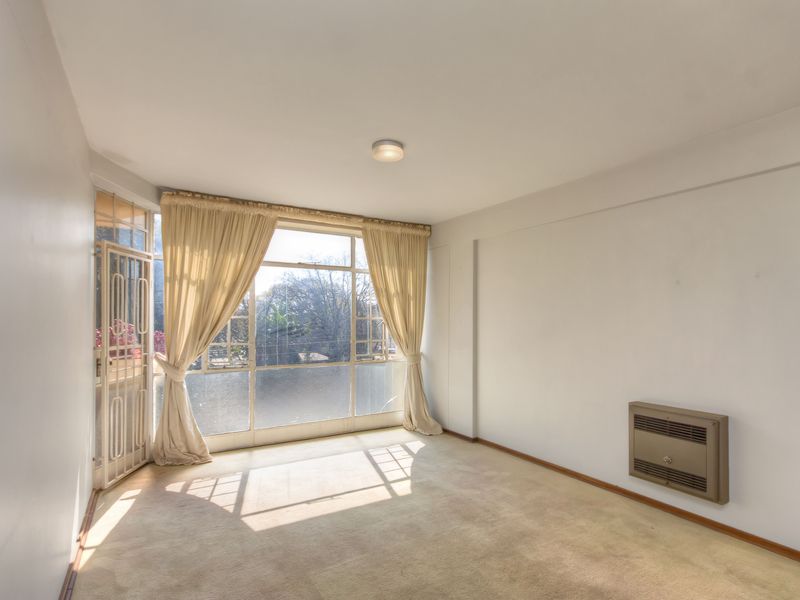 An empty living room featuring a large window, security gate, and wall-mounted heater, offering a bright and versatile space for renovation.