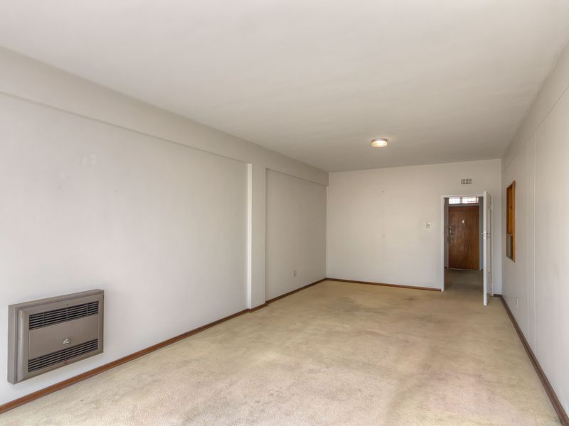An empty, carpeted living room featuring a wall-mounted gas heater and neutral wall finishes, providing a blank canvas for potential renovation or interior design.