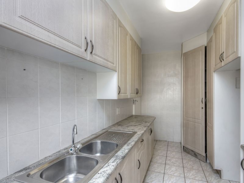 A functional kitchen featuring light wood-toned cabinetry, granite countertops, a stainless steel double sink, and neutral ceramic tile flooring.