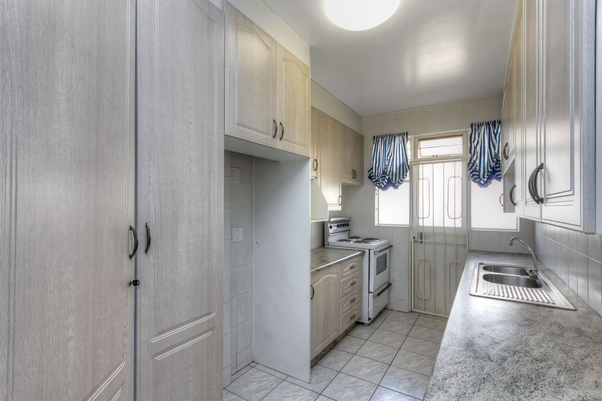 Functional kitchen featuring ample built-in cabinetry, laminate countertops, a stainless steel double sink, and a freestanding stove with direct access to an exterior door.