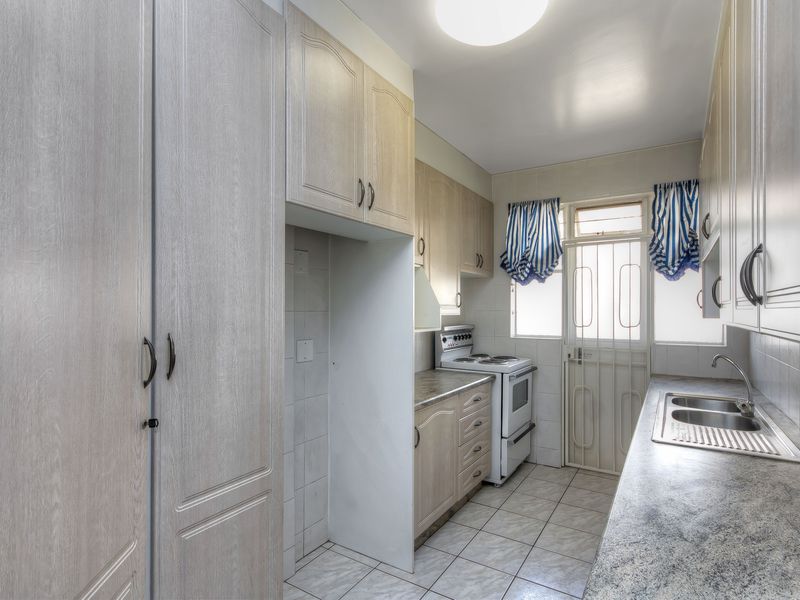 Functional kitchen featuring ample built-in cabinetry, laminate countertops, a stainless steel double sink, and a freestanding stove with direct access to an exterior door.