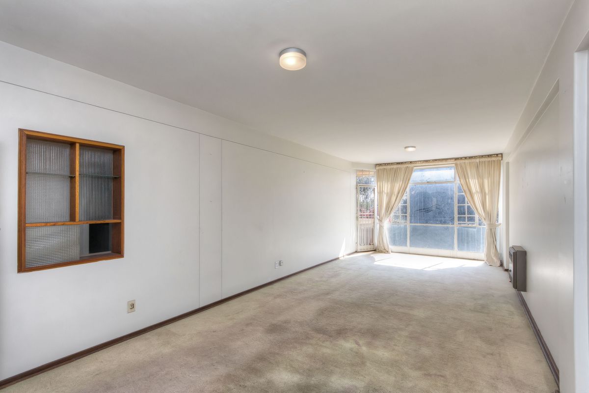 An empty living room featuring carpet flooring, a built-in wall shelf, and large windows allowing natural light.