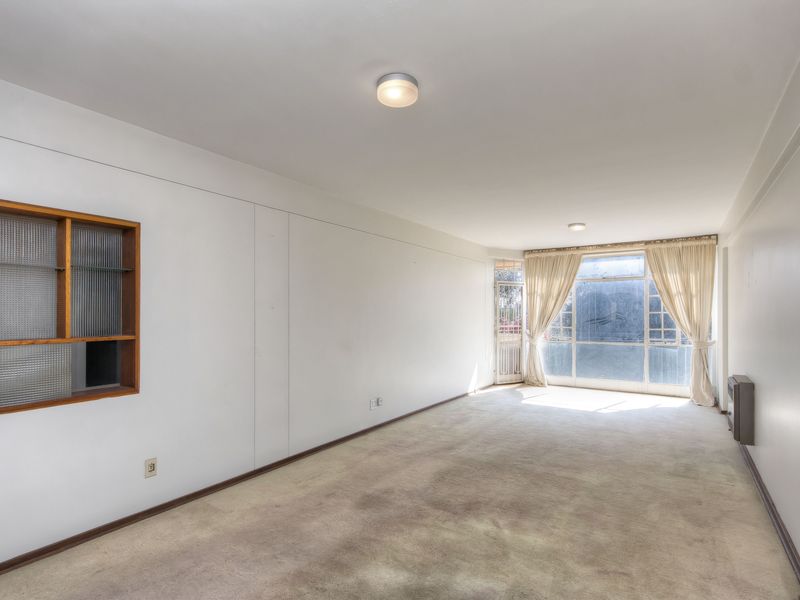 An empty living room featuring carpet flooring, a built-in wall shelf, and large windows allowing natural light.