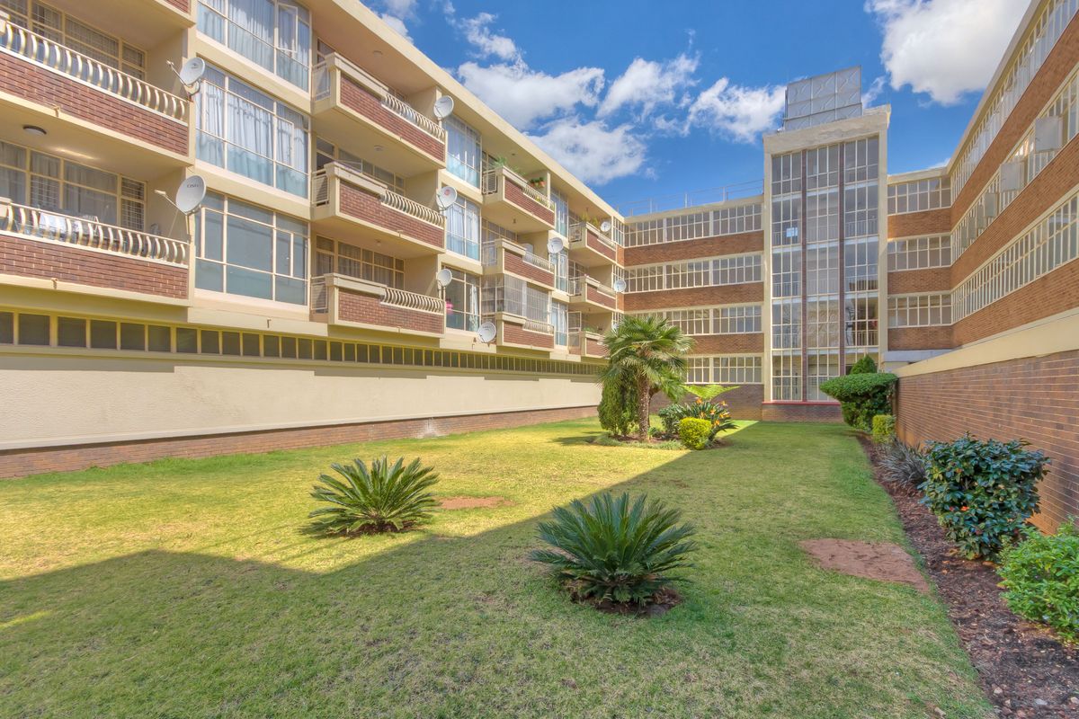 A view of the apartment building's rear facade featuring brick construction, multiple balconies, and a shared communal garden area.