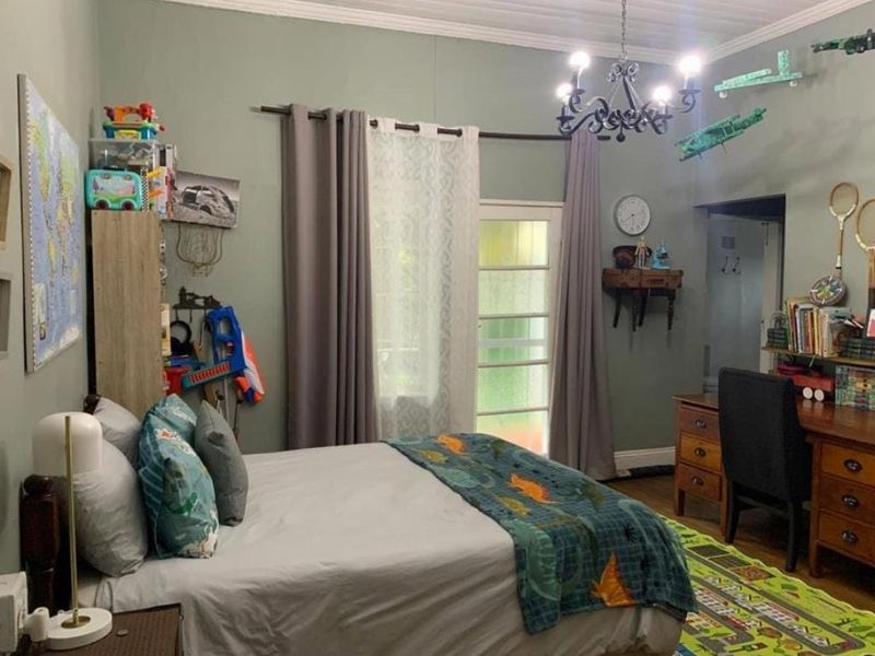 A well-maintained bedroom featuring timber flooring, a classic chandelier, and a glass panel door providing natural light.