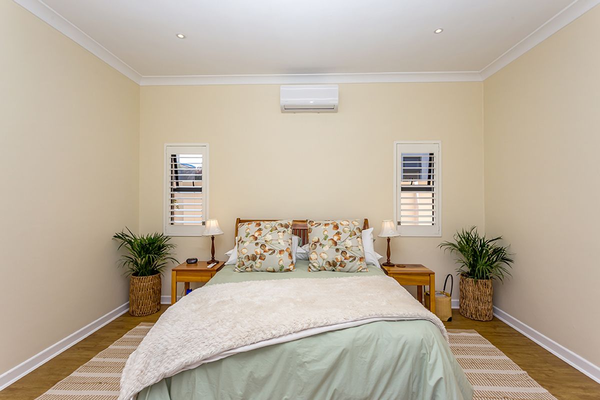 A well-maintained bedroom featuring neutral walls, timber-look flooring, plantation shutters, and a wall-mounted split-system air conditioner.