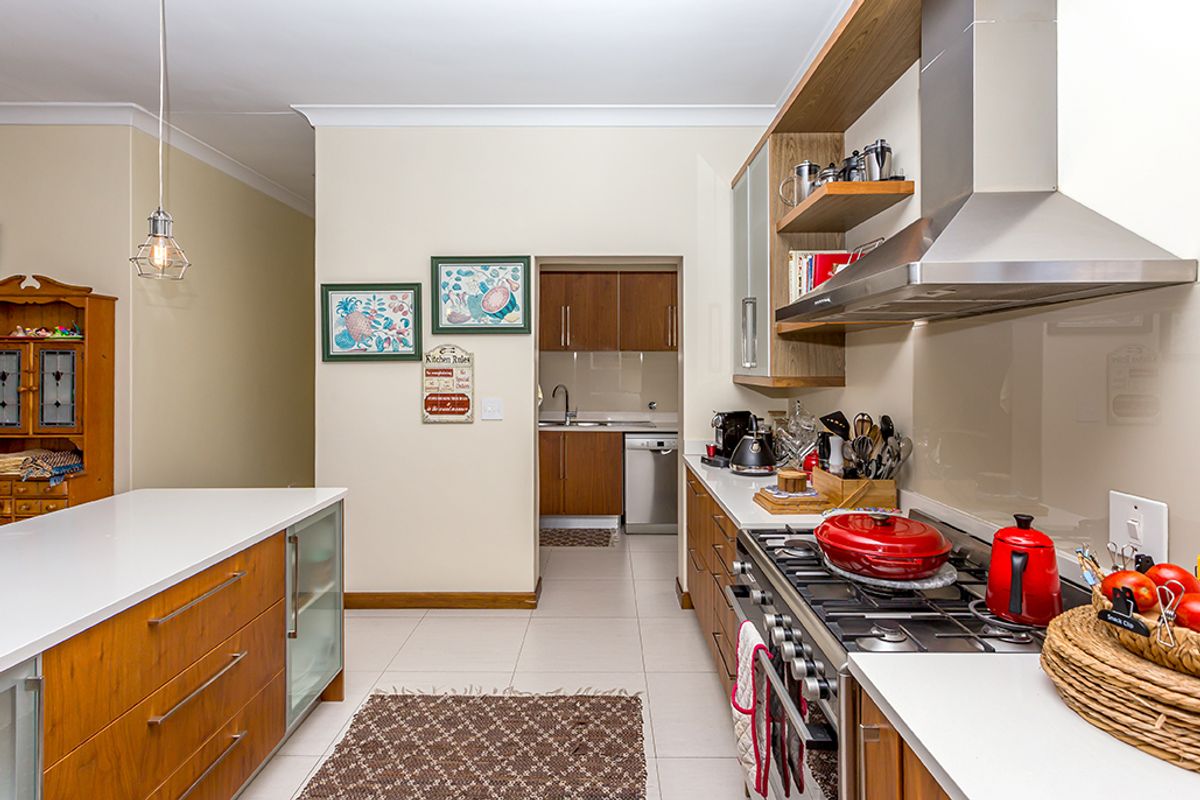 Modern kitchen featuring a central island, gas cooktop with stainless steel extractor, stone countertops, and an adjoining scullery area.